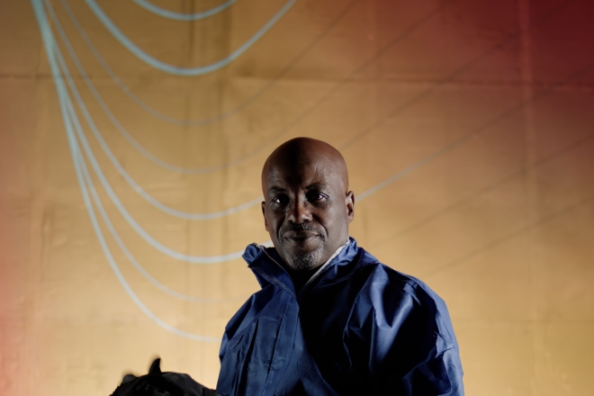 Person in a blue PPE jacket standing in front of a red-to-yellow gradient background with light blue curved lines