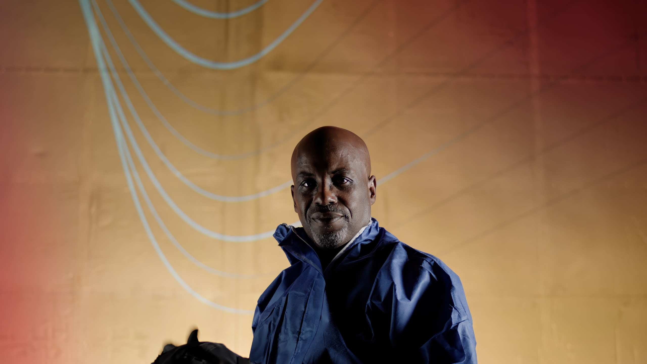 Person in a blue PPE jacket standing in front of a red-to-yellow gradient background with light blue curved lines