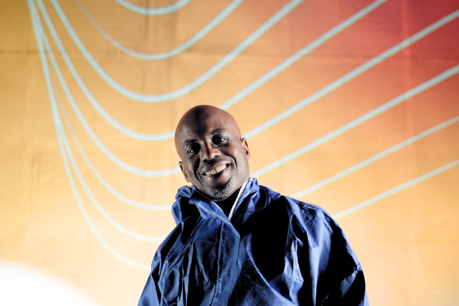 Person in a blue protective suit and black gloves holding a virtual reality headset above their head, with curved illuminated lines in the dark background.