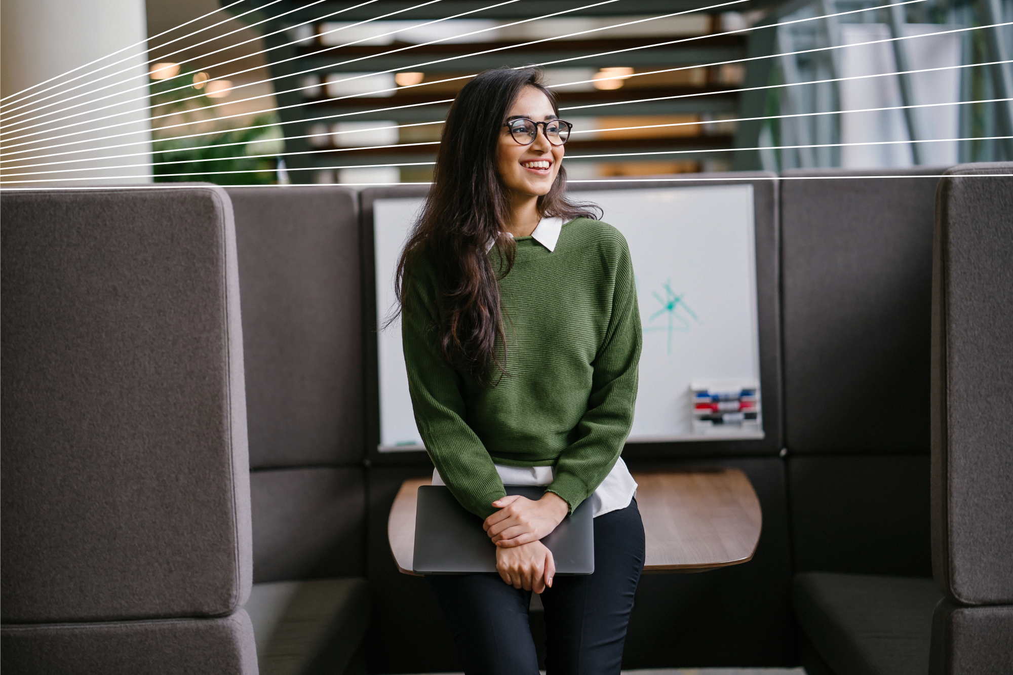 Portrait of a young woman student smiling as she leans in a discussion booth in her campus. She is wearing a green jumper.