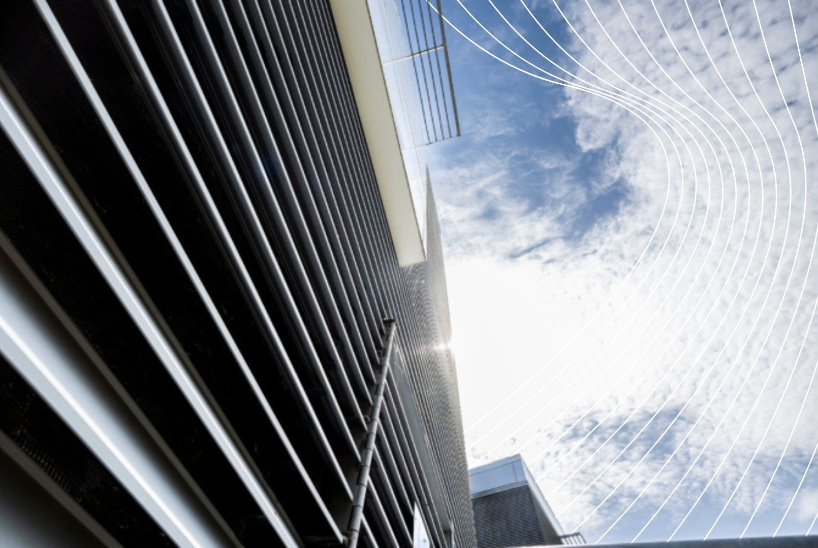 Upward view of a modern building with horizontal metal slats on its facade, set against a bright sky with scattered clouds and white curved graphic lines overlaying the sky.