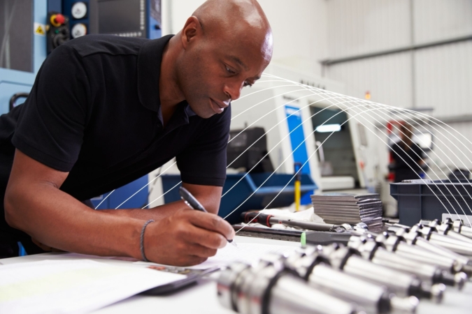 Engineer Planning Project With CNC Machinery In Background