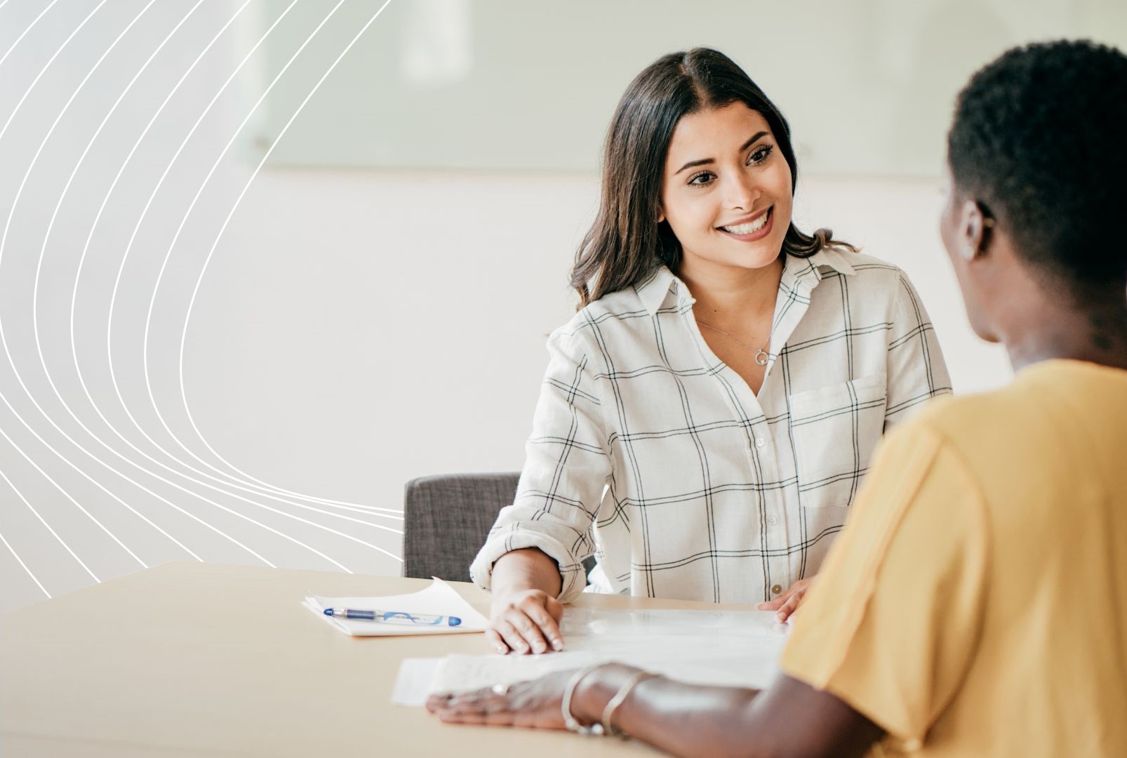 Two people seated at a table in a professional setting, discussing documents on a clipboard—suggesting a job interview or career opportunity.