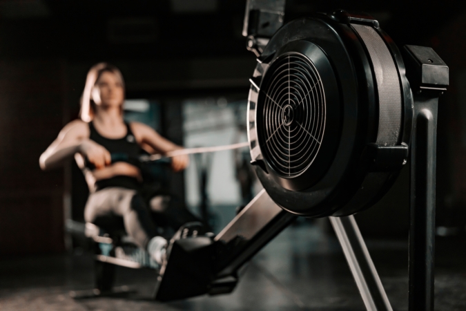 Woman doing rowing exercises on fitness machine in gym. Selective focus on machine.
