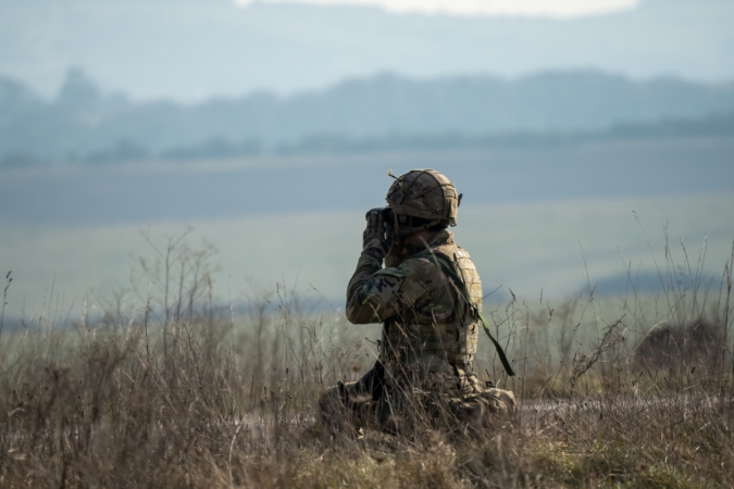 close-up of a British army infantry soldier using binoculars to scan distance for enemy threats, military exercise, Wiltshire UK