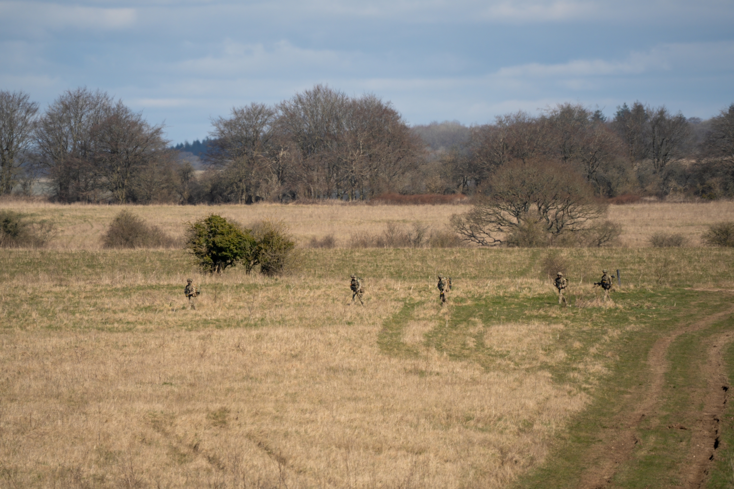 British army infantry soldiers moving moving across an early spring in sunshine