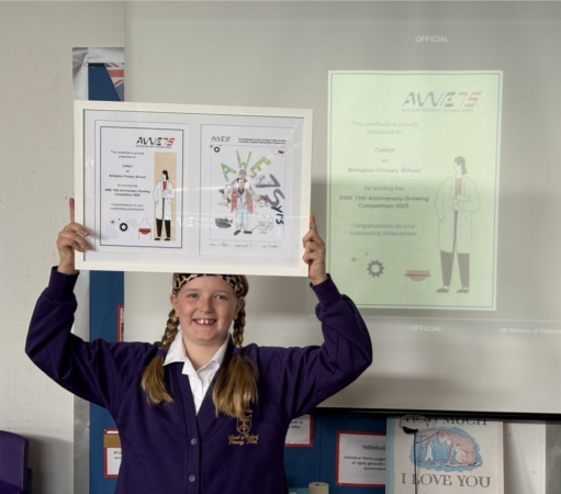 Caitlyn from Brimpton Primary School with her winning artwork held up above her head with a big smile on her face